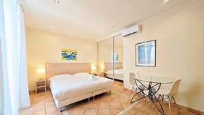 A hotel room with a bed, bedside tables, a desk with a chair, a mirror, and artwork on the walls. - Studio Commandant André 33 by Viva Riviera (Cannes)