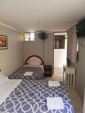 A bedroom with two beds, a ceiling fan, a small table, and a TV on the wall.