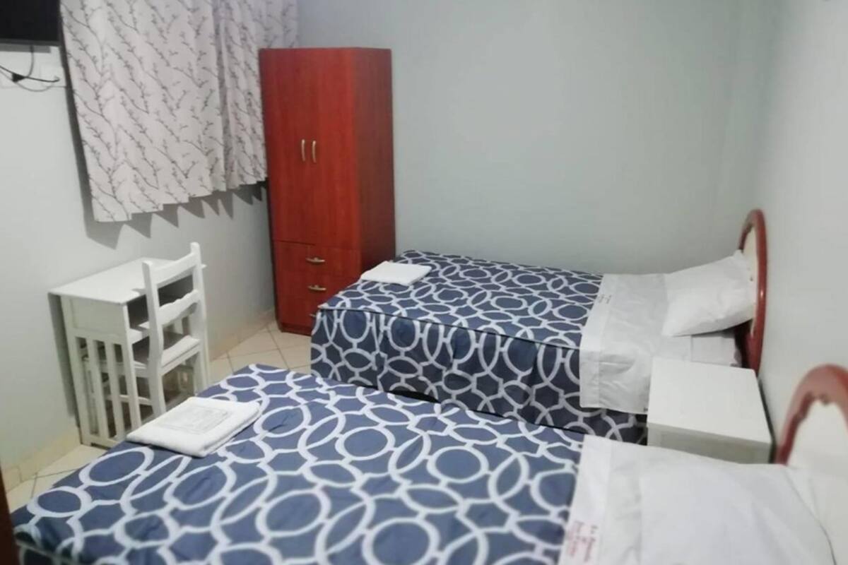Un dormitorio pequeño y ordenado con dos camas individuales, un armario de madera y una mesita de noche blanca.