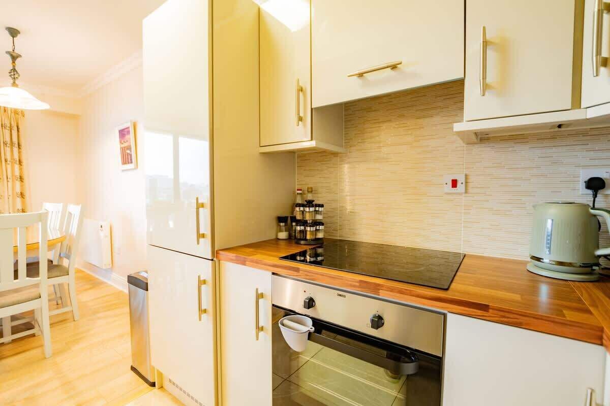 A modern kitchen with white cabinets, a wooden countertop, a built-in oven, and a kettle.