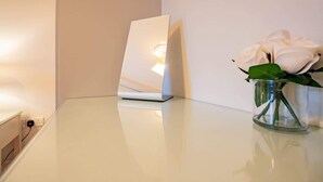 Une table blanche avec un ordinateur portable, un vase contenant une rose blanche et une prise de courant au mur.