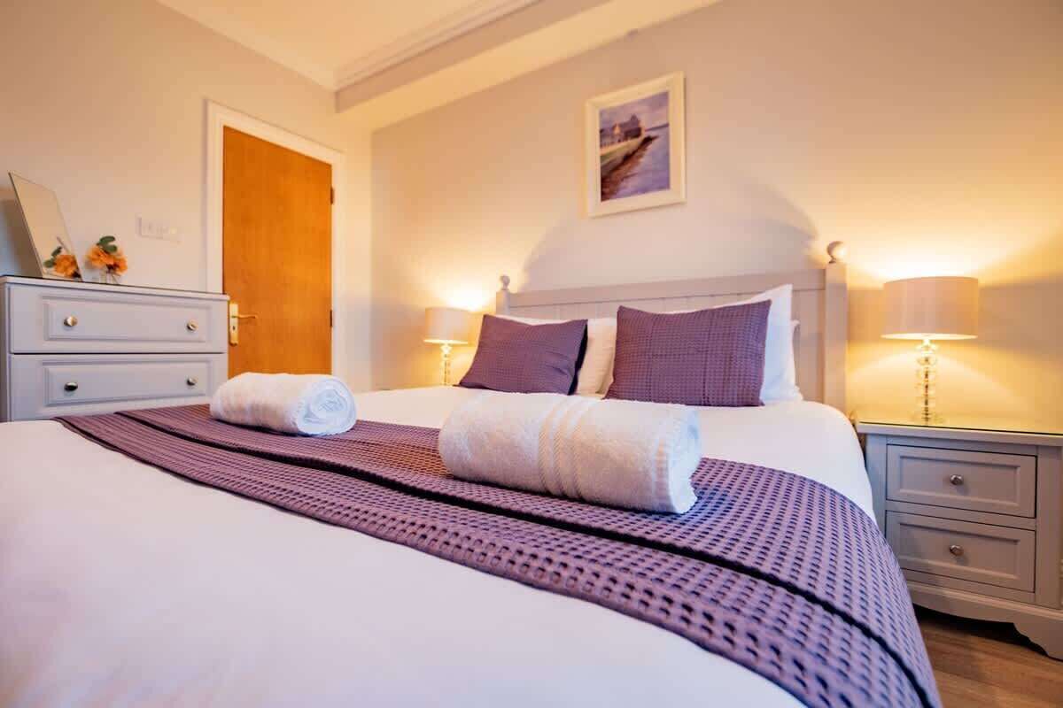A hotel room with a large bed, two bedside tables, a nightstand, a door, and a framed picture on the wall.