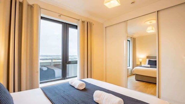 Une chambre d’hôtel avec un grand lit, une vue sur la ville par la fenêtre et un miroir qui reflète la pièce.