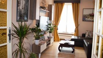 Un salon moderne avec une table basse en bois, un canapé noir et un téléviseur posé sur un meuble en bois. On y trouve également des plantes en pot et un tableau accroché au mur.