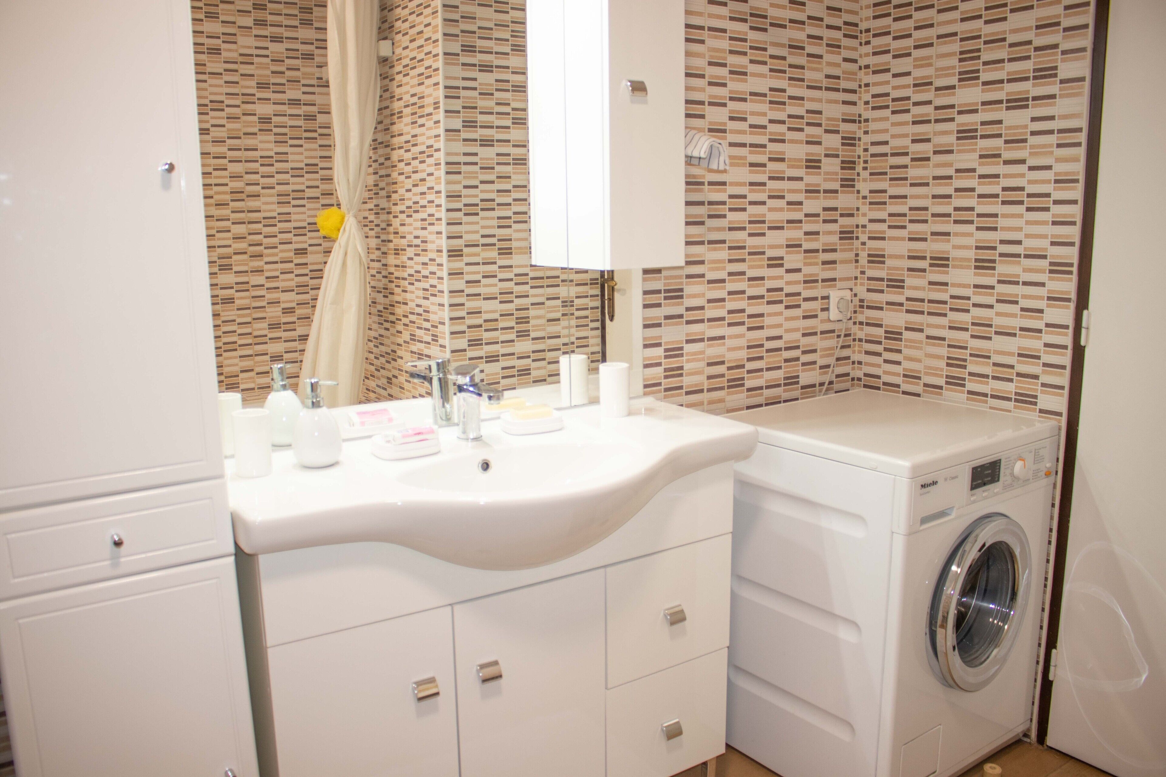A bathroom with a sink, mirror, and washing machine.