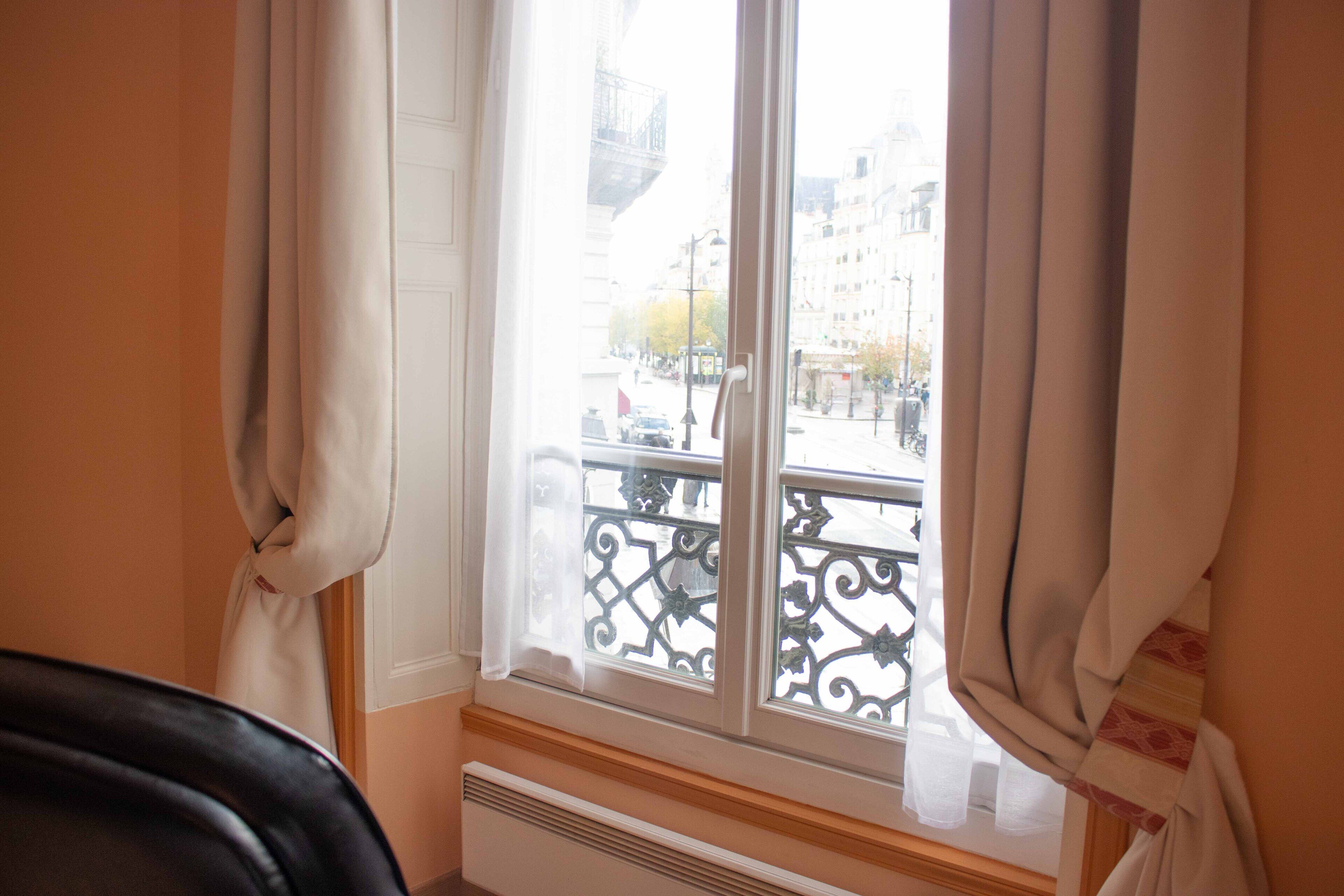 A room with a window overlooking a street, a radiator below the window, and a chair in the foreground.