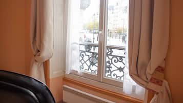 A room with a window overlooking a street, a radiator below the window, and a chair in the foreground.