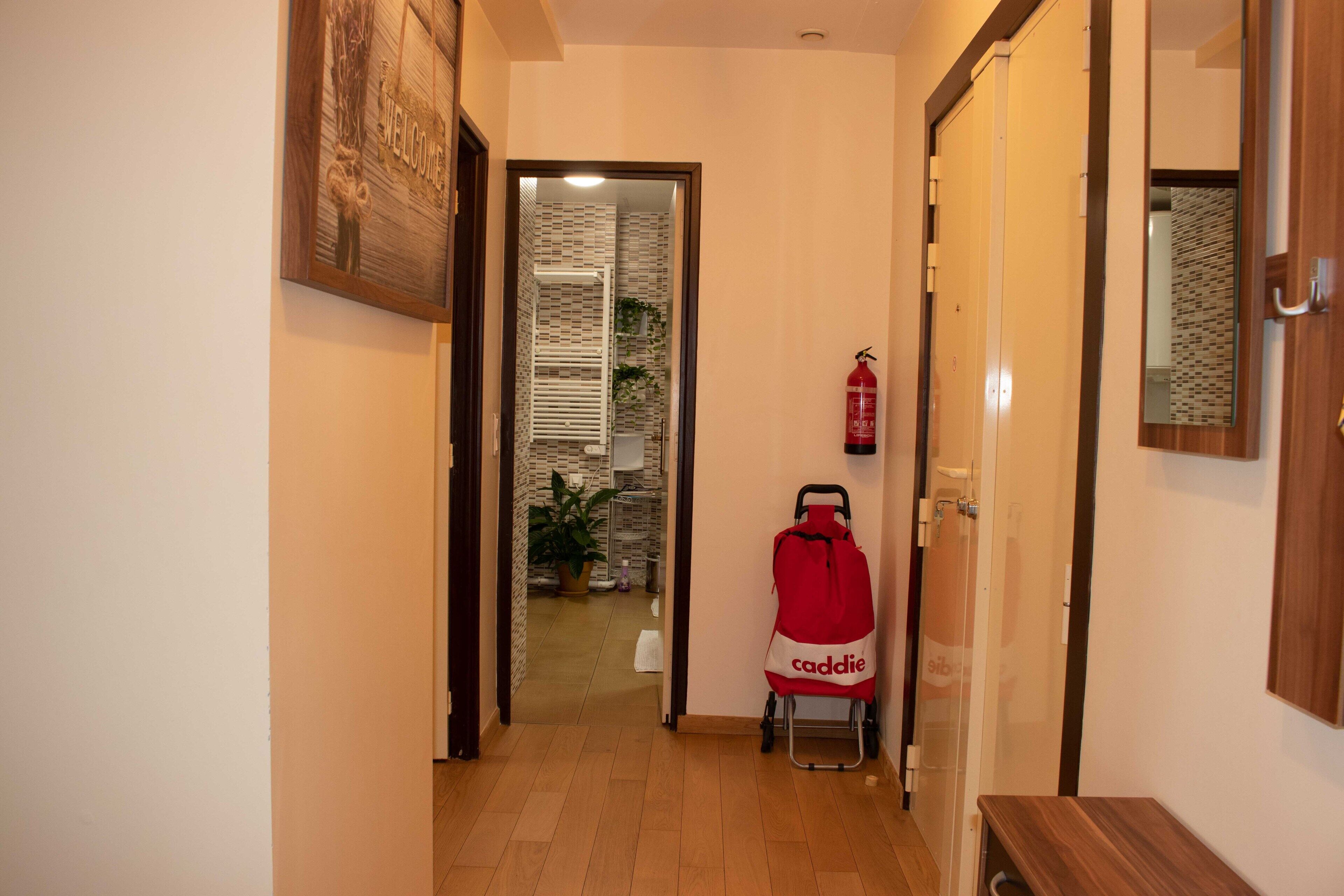 A hallway with a fire extinguisher, a red bag, and a mirror on the wall.