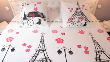 Un lit avec une literie blanche et des coussins décoratifs représentant la Tour Eiffel et des fleurs.