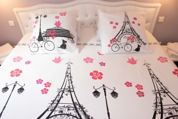 A bed with white bedding and decorative pillows featuring the Eiffel Tower and flowers.