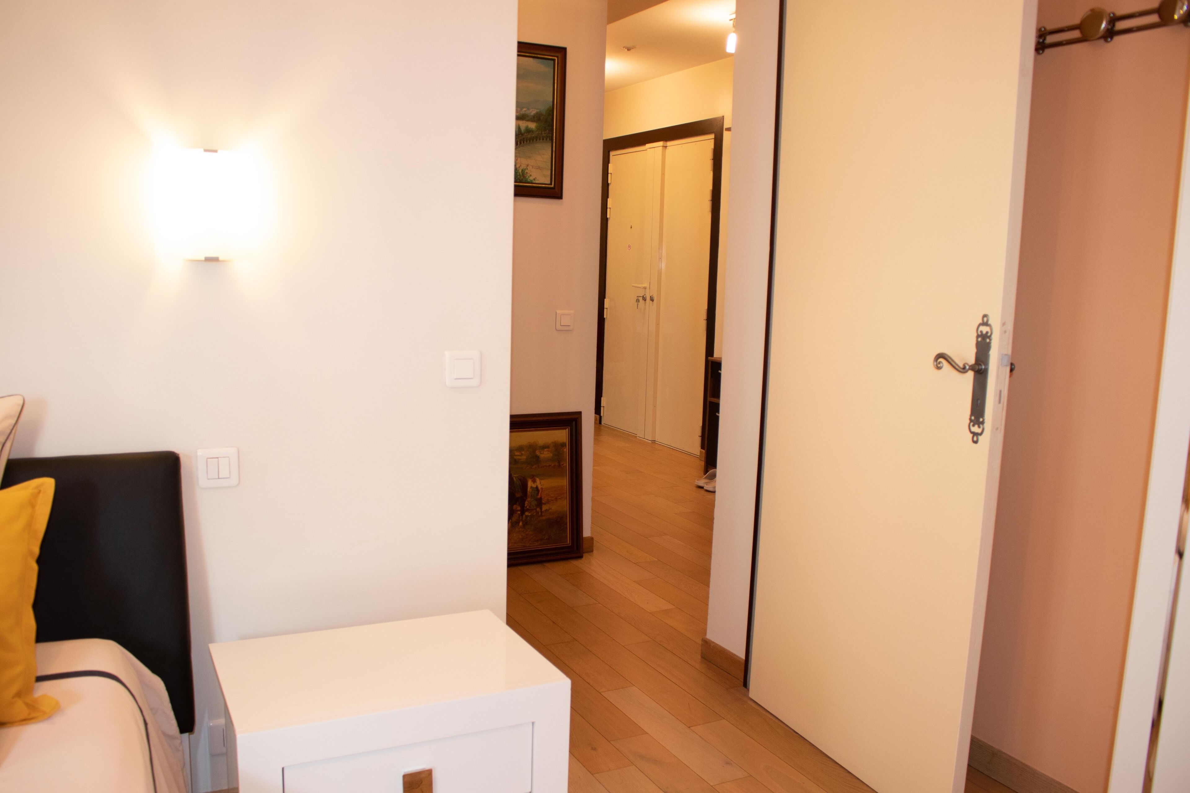 Une chambre d’hôtel comprenant un lit, une table de chevet, une armoire et un couloir menant à une autre pièce.