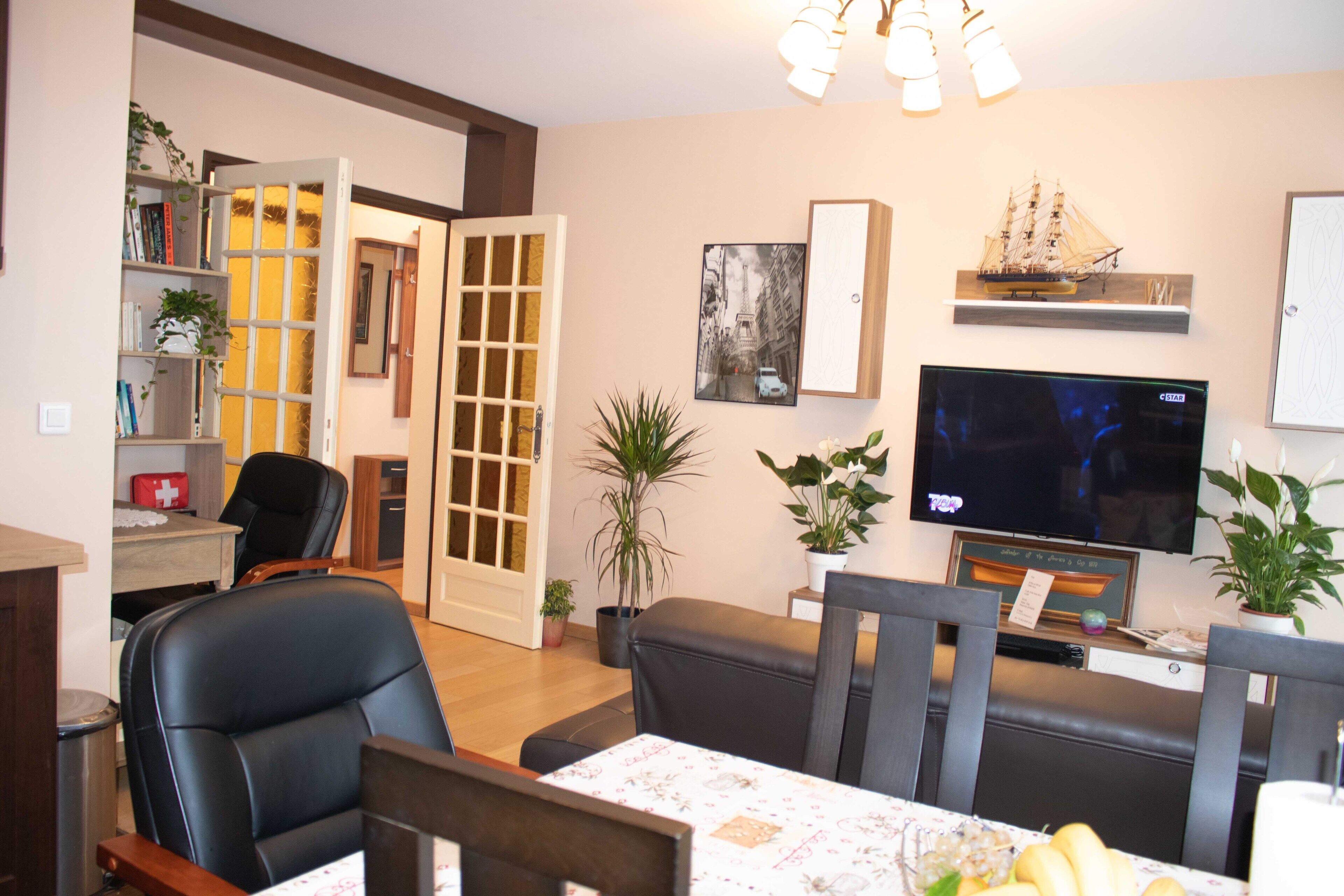 A living room with a dining table, chairs, a television, and a bookshelf.