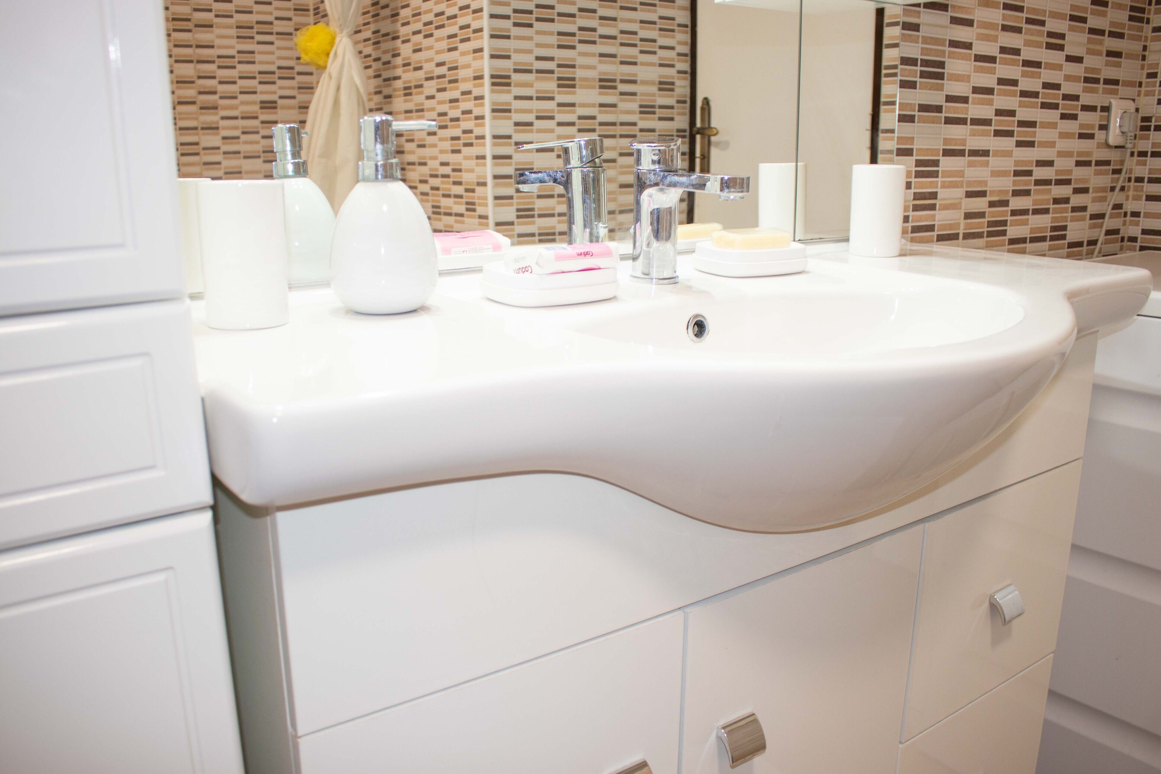 A modern bathroom with a white sink, chrome faucets, and a tiled backsplash.
