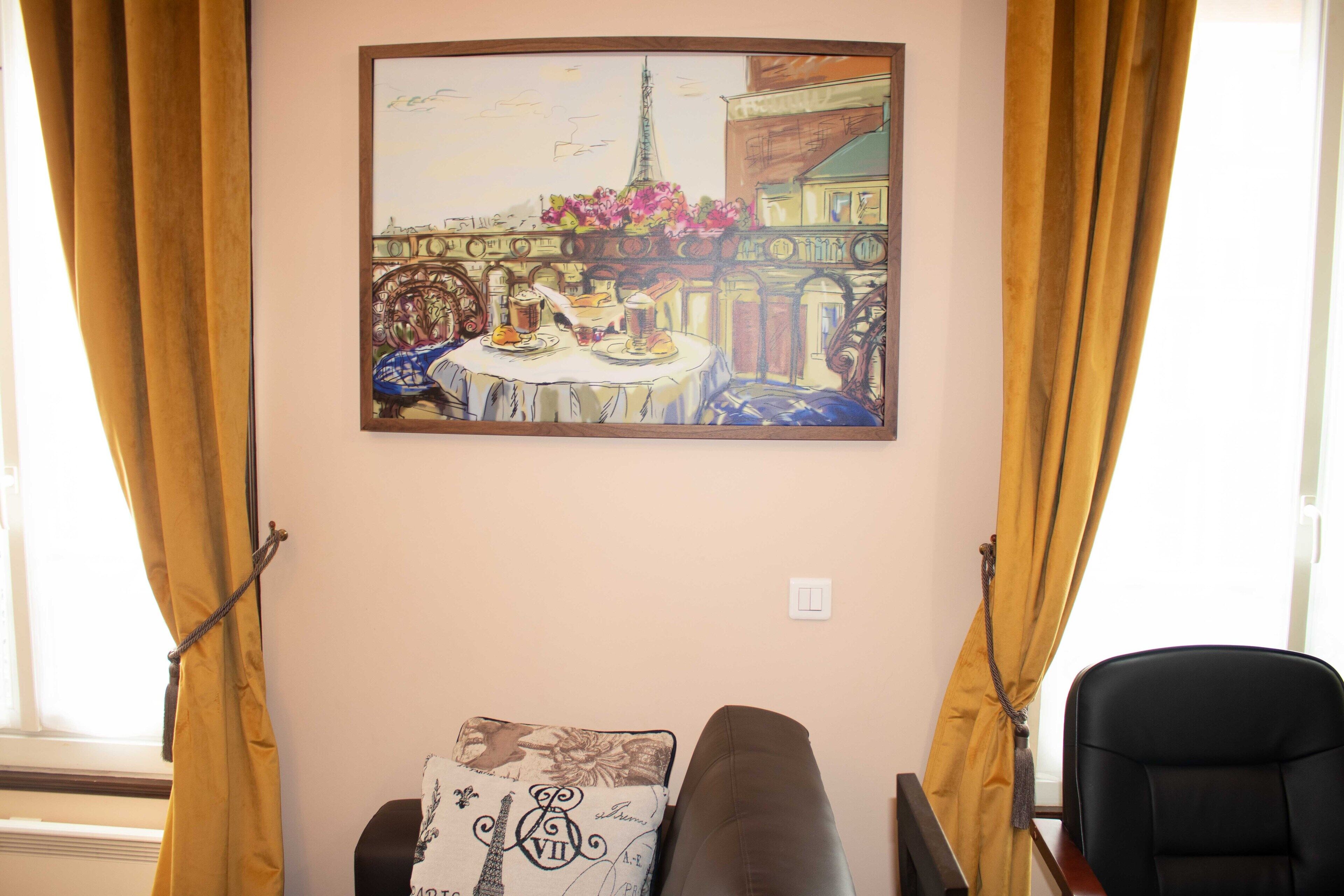 A room with a painting of a Parisian street scene, a window with curtains, a sofa with a decorative pillow, and a chair.
