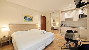 A hotel room with a large bed, a desk with a chair, a television mounted on the wall, a microwave, and a washing machine. - Studio Commandant André 13 by Viva Riviera (Cannes)