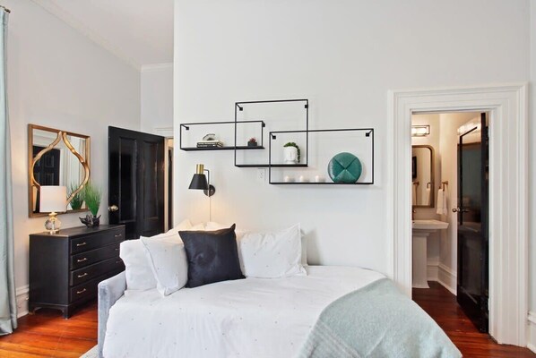 A bedroom with a bed, a dresser, a mirror, and wall-mounted shelves with decorative items.