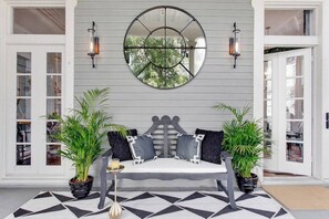 A room with a bed, two potted plants, a round mirror, and two wall sconces.
