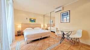 Habitación de hotel con una cama grande, un escritorio con silla, un espejo y un cuadro de Cannes en la pared.