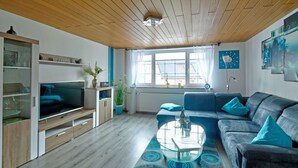 Een moderne woonkamer met een houten plafond, een bank, een salontafel en een televisie.