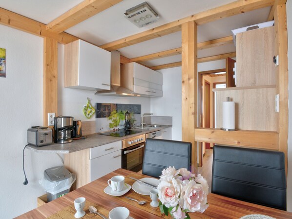 A modern kitchen with wooden beams, white cabinets, a dining table with chairs, and a vase of flowers.