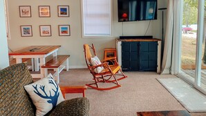 Un salon avec une table en bois, un fauteuil à bascule et un téléviseur fixé au mur.