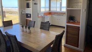A modern kitchen with white cabinets, a wooden dining table, and a view of the beach. - Classic Shack -  Absolute Beachfront.  Winter off peak special! (Point Turton)