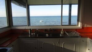 A kitchen with a large window overlooking the sea, a sink, and cabinets. - Classic Shack -  Absolute Beachfront.  Winter off peak special! (Point Turton)