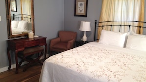 A bedroom with a bed, a chair, a desk, a lamp, and a mirror.