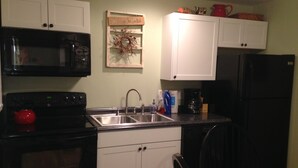 A kitchen with white cabinets, a black microwave, a red kettle, and a sink with a faucet.