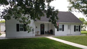 A single-story house with a front porch, a small table and chairs, and a flag.