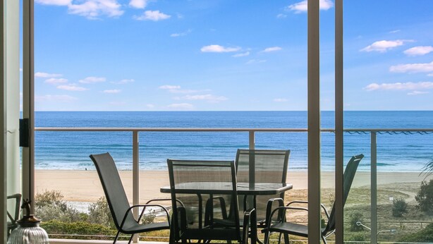 Un balcón con mesa y sillas con vistas a una playa y al océano.