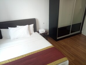 A neatly made bed with white bedding and a red and yellow striped blanket. There is a small bedside table with a white towel and a remote control. A sliding closet door is visible to the right of the bed. - Taragon Time Executive Serviced Suites (Kuala Lumpur)