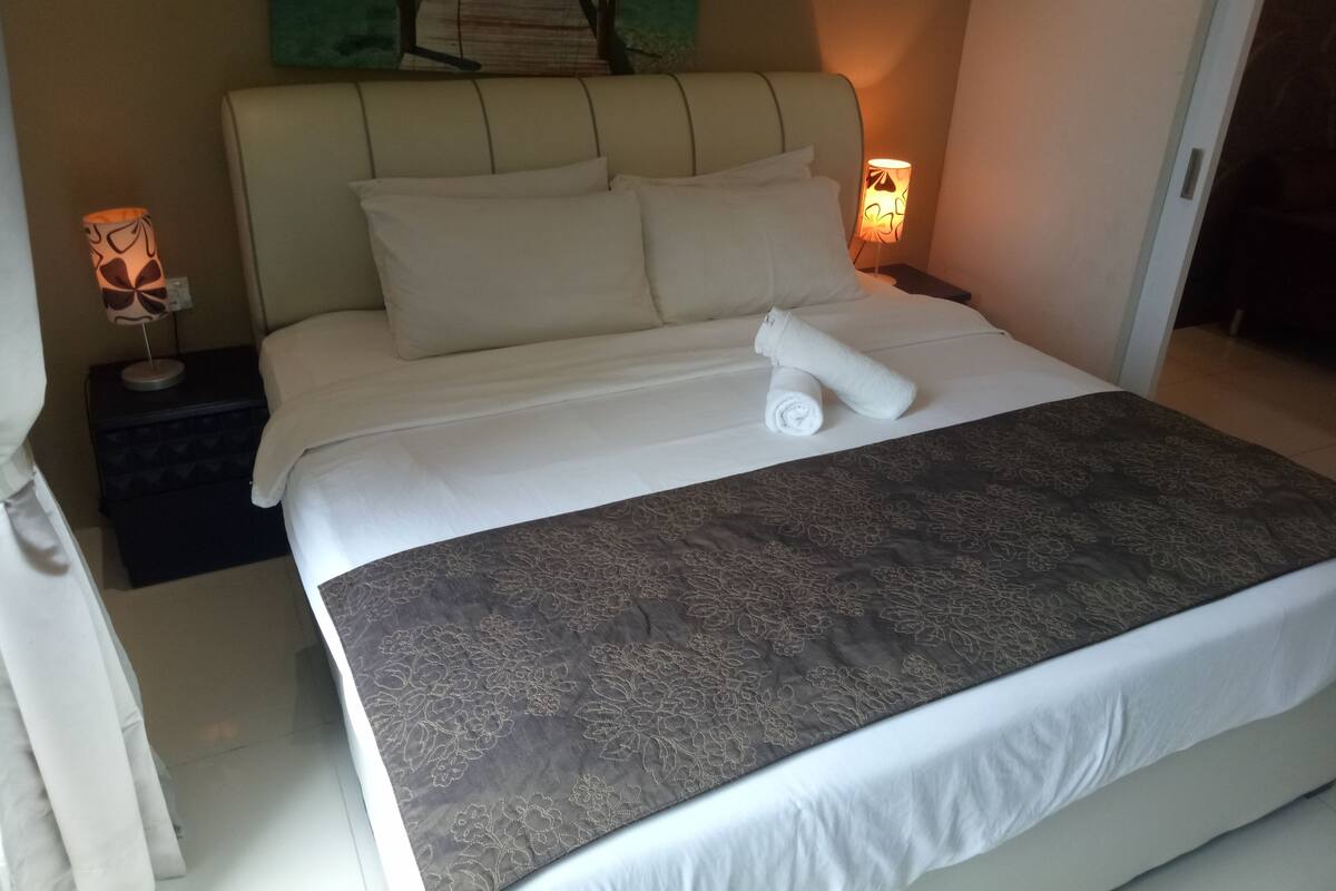 A neatly made bed with a floral-patterned bedspread, a headboard, and two bedside lamps.