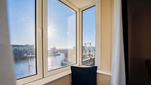 A room with a large window overlooking a harbor, a dark blue pillow, and a white curtain. - Stylish Harbour View Apartment in a Private Building (Galway City)