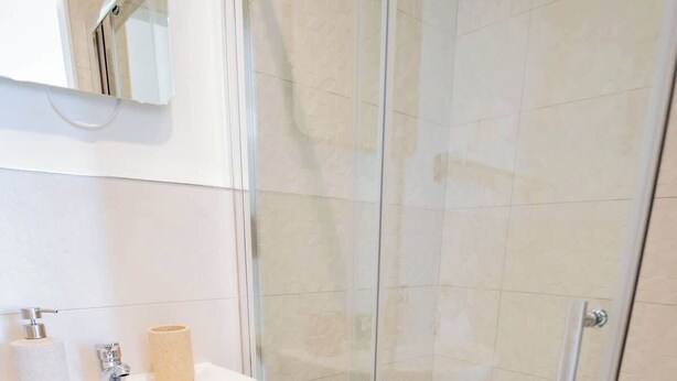 A modern bathroom with a glass shower enclosure, a pedestal sink, and a mirror above the sink. - Stylish Harbour View Apartment in a Private Building (Galway City)