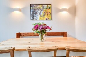 Uma mesa de jantar com um vaso de flores, cadeiras de madeira e duas luzes fixadas na parede.