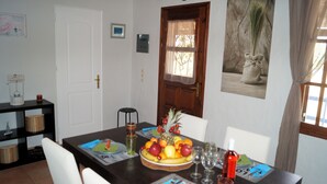 Ein Esstisch gedeckt mit Obst, Weingläsern und einer Flasche, mit einer Holztür und einem gerahmten Bild an der Wand.