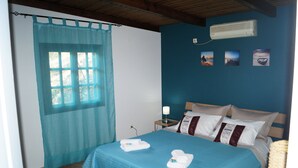 Ein Schlafzimmer mit einem Bett, einem Fenster mit Vorhang, einer Wand-Klimaanlage und drei gerahmten Bildern.