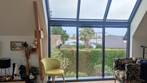 Quarto com um amplo claraboia, uma cadeira amarela, um sofá estampado e vista para uma área residencial.