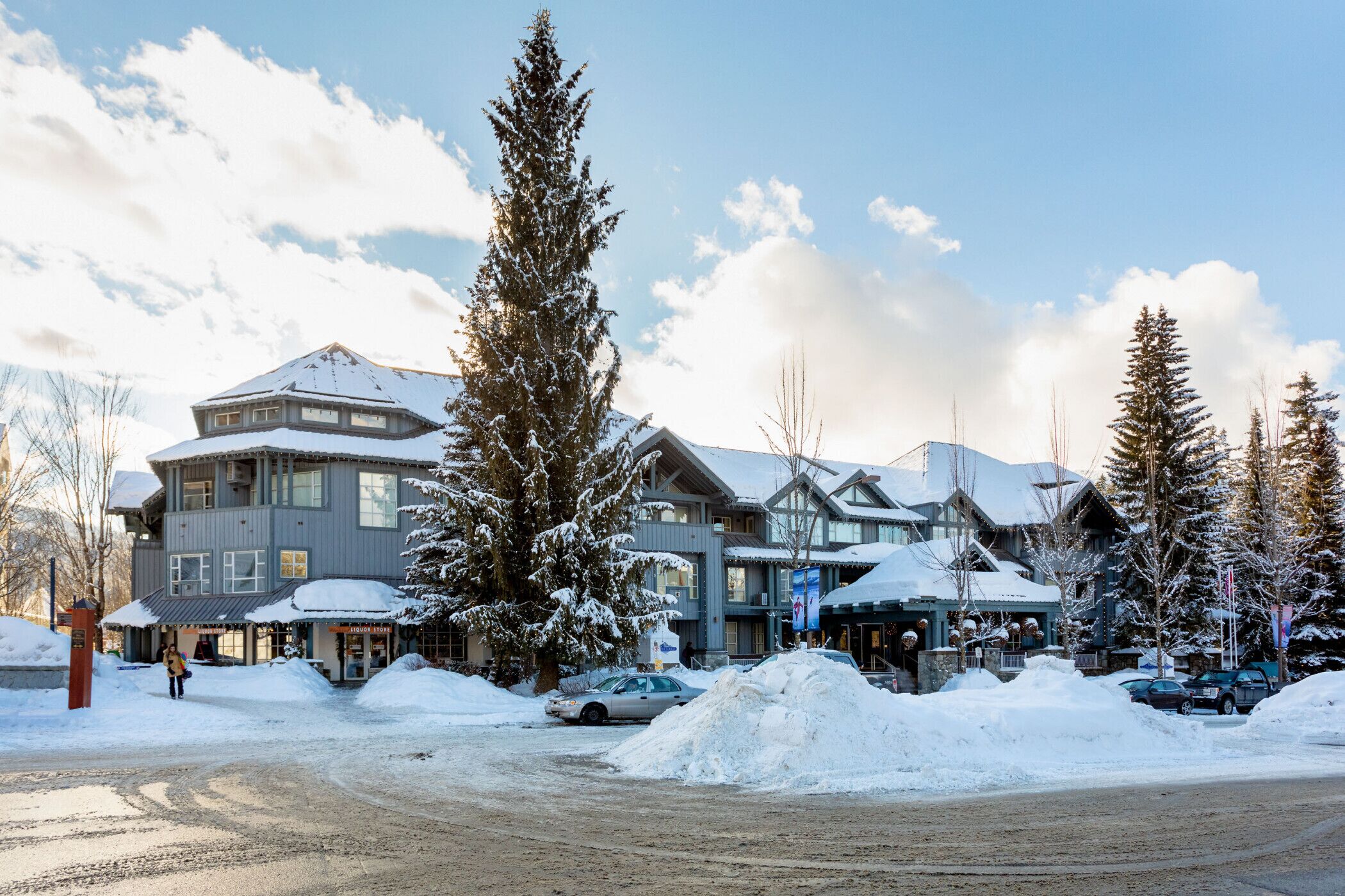 Ein großes Chalet mit mehreren Gebäuden, einem verschneiten Parkplatz und hohen Nadelbäumen.