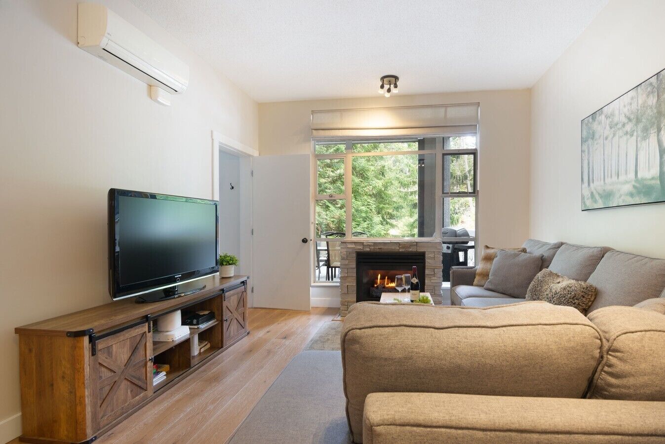 Sala de estar con televisor, sofá, chimenea y vistas al exterior.