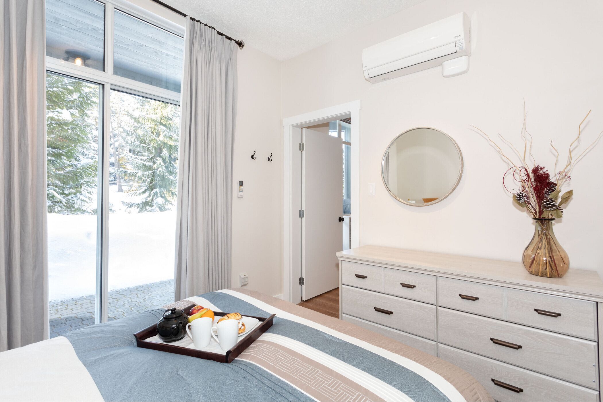 Habitación de hotel con cama, cómoda, espejo y ventana con cortinas.