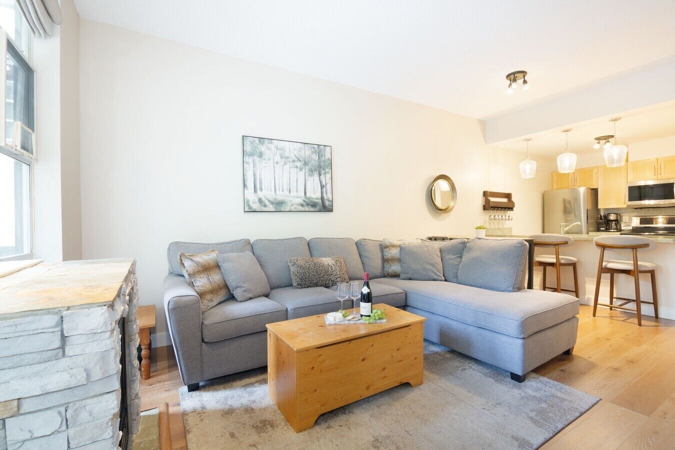 Ein modernes Wohnzimmer mit einem grauen Ecksofa, einem Couchtisch aus Holz und einer Küchenzeile mit Barhocker.