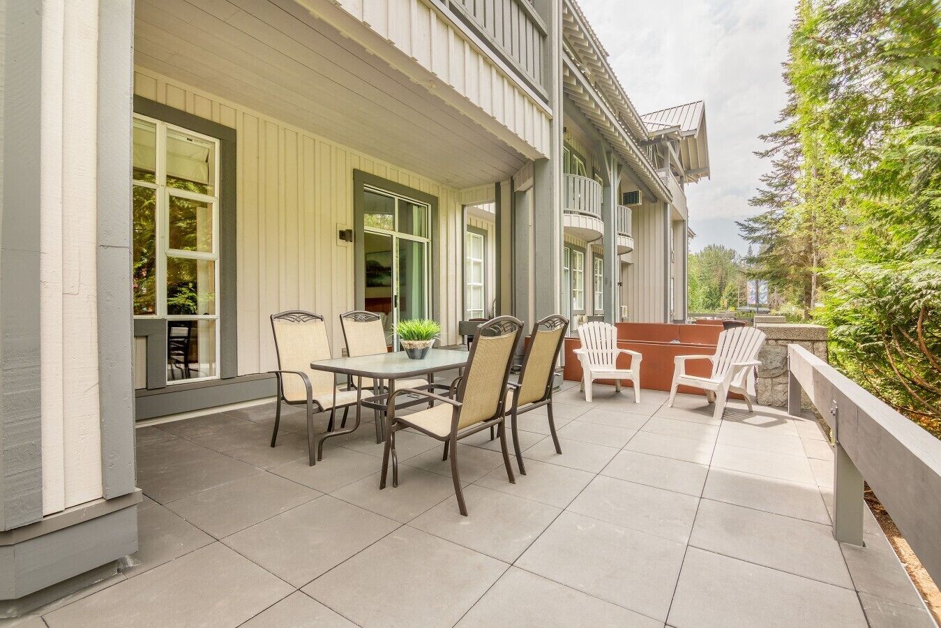 A patio with a table and chairs, a potted plant, and a view of a forested area.