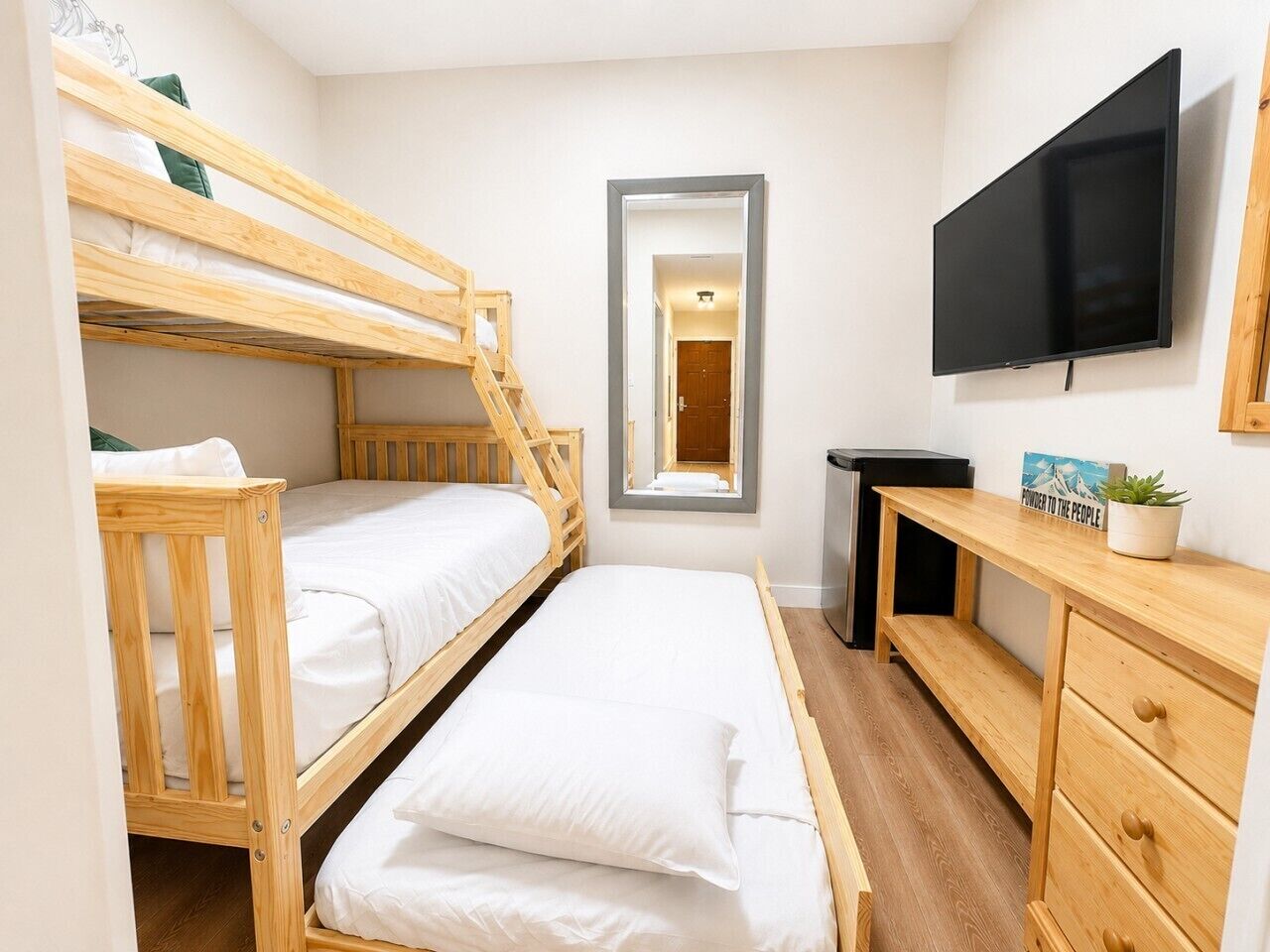 Een slaapkamer met stapelbedden, een bureau, een televisie en een spiegel.