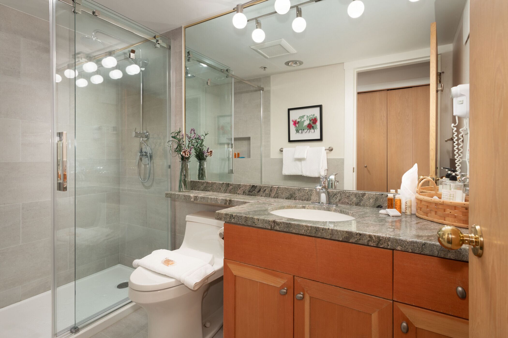 Un baño moderno con cabina de ducha de vidrio, inodoro blanco, lavabo con encimera de mármol y armarios de madera.