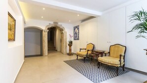 A spacious hallway with a patterned rug, two armchairs, a small table, and a staircase leading to another room.