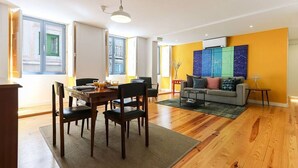 A spacious living room with a dining area, wooden flooring, and large windows.