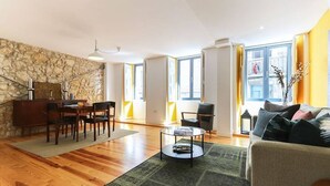 A modern living room with a stone accent wall, a dining area with a wooden table and chairs, a round coffee table, and a sofa with cushions.