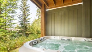 Un bain à remous avec une terrasse en bois et vue sur une forêt.